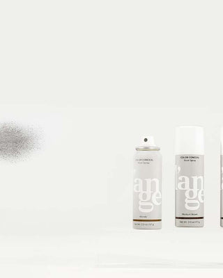 A hand spraying a can of root concealer with other cans and applicators lined up beside it, displaying a range of hair touch-up products.