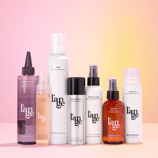 Assorted L’ange hair care bottles on a pink-to-gold gradient background