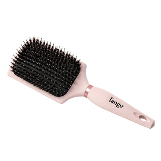 The pink boar bristle brush sits diagonally, showing its handle, the logo, and paddle.