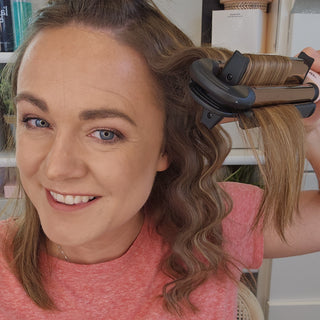 Woman smiling while using a hair waver to create soft curls, showcasing the styling tool in action.