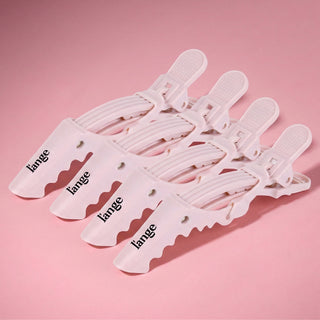 Four pink L'ange alligator hair clips arranged on a smooth pink background