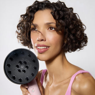 model with dark defined curly hair holding the Axia hair dryer and diffuser
