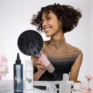 model with curly hair holding the Axia dryer and various hair care