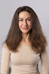 A person with long, voluminous brown hair wearing a beige top smiles against a plain background.