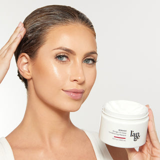 Person applying Borago Oil Deep Conditioning Masque to hair, holding a 10 fl oz jar labeled "l’ange." Skin glows under soft lighting, with focus on hydrating hair treatment product.