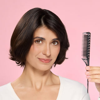 Woman holding a black teasing pin tail comb against a pink background.