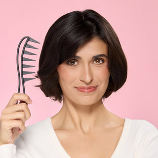 Woman holding a wide tooth comb against a pink background.