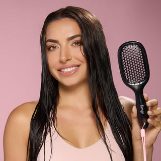 Model with wet hair smiling and holding L’ange black detangling brush against pink background