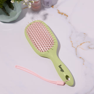 L’ange green and pink detangling hair brush on a vanity with hair products 