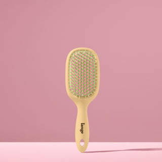 yellow and green L’ange detangling brush standing upright on pink background