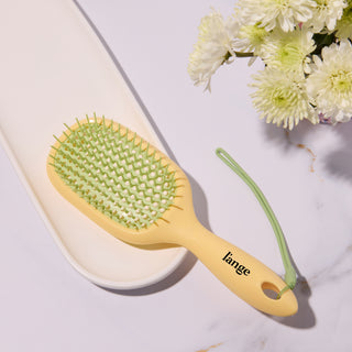 L’ange yellow and green detangling hair brush on a vanity 