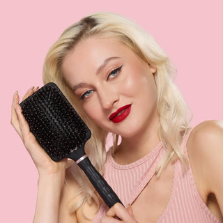 Model smiling while holding a black detangling paddle brush with boar