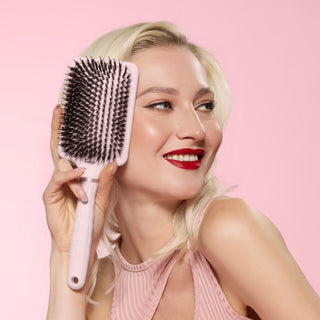 Model smiling while holding a blush detangling paddle brush with boar
