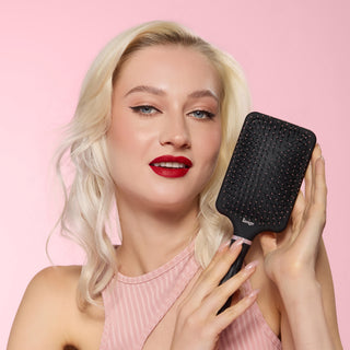Model smiling while holding a black detangling paddle brush 