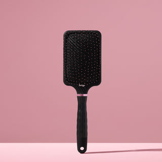 black L’ange detangling paddle brush with nylon bristles standing upright on pink background