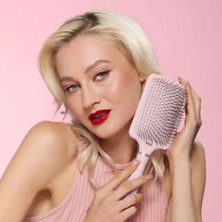 Model smiling while holding a blush detangling paddle brush 