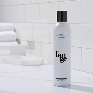 L’ange Détox Balancing Charcoal Conditioner displayed on a bathroom counter with towels and a perfume bottle.