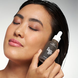 Woman with wet hair holding a bottle of L’ange Détox Scalp Reset Serum close to her face.