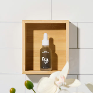 L’ange Détox Scalp Reset Serum bottle displayed in a wooden shelf against white tiled wall.