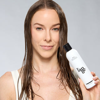 Woman with wet hair holding a bottle of L’ange Détox Deep-Cleansing Charcoal Shampoo.
