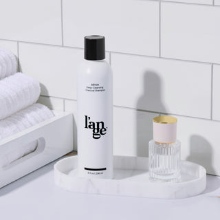 L’ange Détox Deep-Cleansing Charcoal Shampoo displayed on a bathroom counter with a perfume bottle and towels.