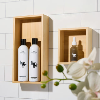 L’ange Détox shampoo, conditioner, and serum displayed on wooden shelves against a tiled bathroom wall.