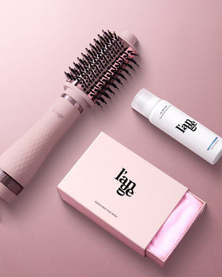 A pink background features a pink hair styling brush, a bottle of hair product, and a box labeled "l'ange Microfiber Hair Wrap" partially open to reveal the fabric inside.