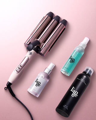 Three-barrel curling iron with sleek design, accompanied by three styling products in white, teal, and black bottles, arranged on a soft pink background.
