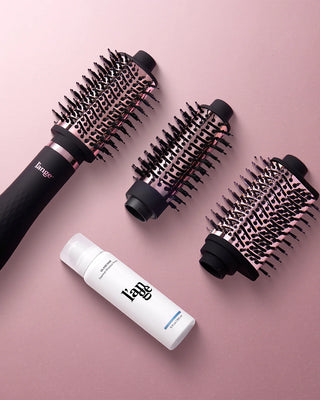 A set of interchangeable round hairbrush attachments and a styling product bottle, all on a pink background.