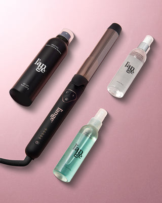 Haircare product selection featuring a styling wand, volumizing spray, thermal protection spray, and texturizing spray on a pink background.