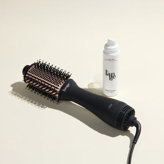 The Effortless Blowout Duo Value Set, featuring a Black Le Volume brush and Glass Hair spray, displayed against a beige background