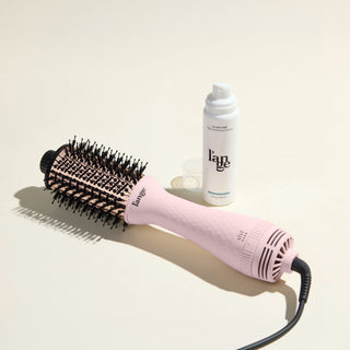 The Effortless Blowout Duo Value Set, featuring a Blush Le Volume brush and Glass Hair spray, displayed against a beige background