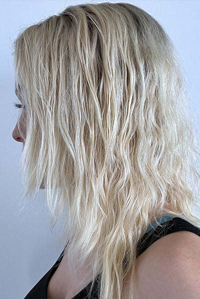 A person with long, slightly wavy blonde hair is shown in profile against a plain background.