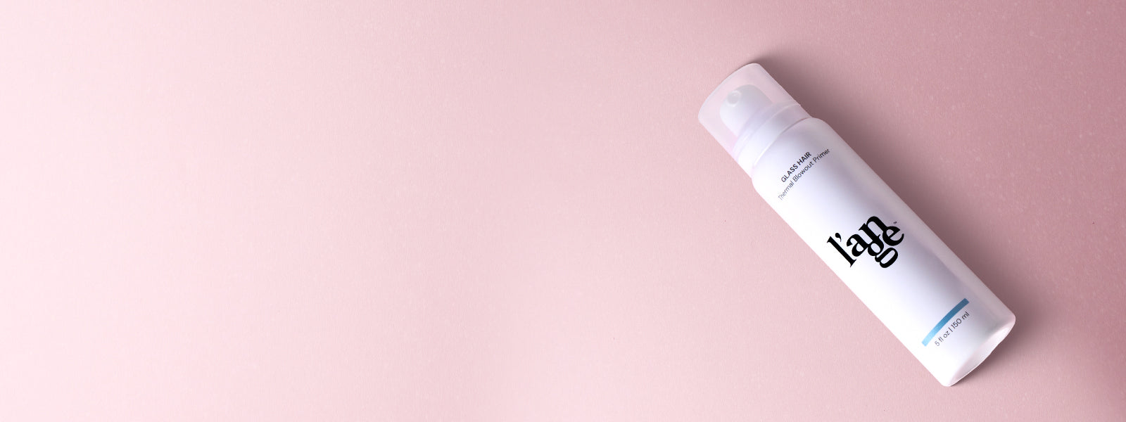A white bottle labeled "l’ange Glass Hair Thermal Blowout Primer," positioned on a soft pink background.