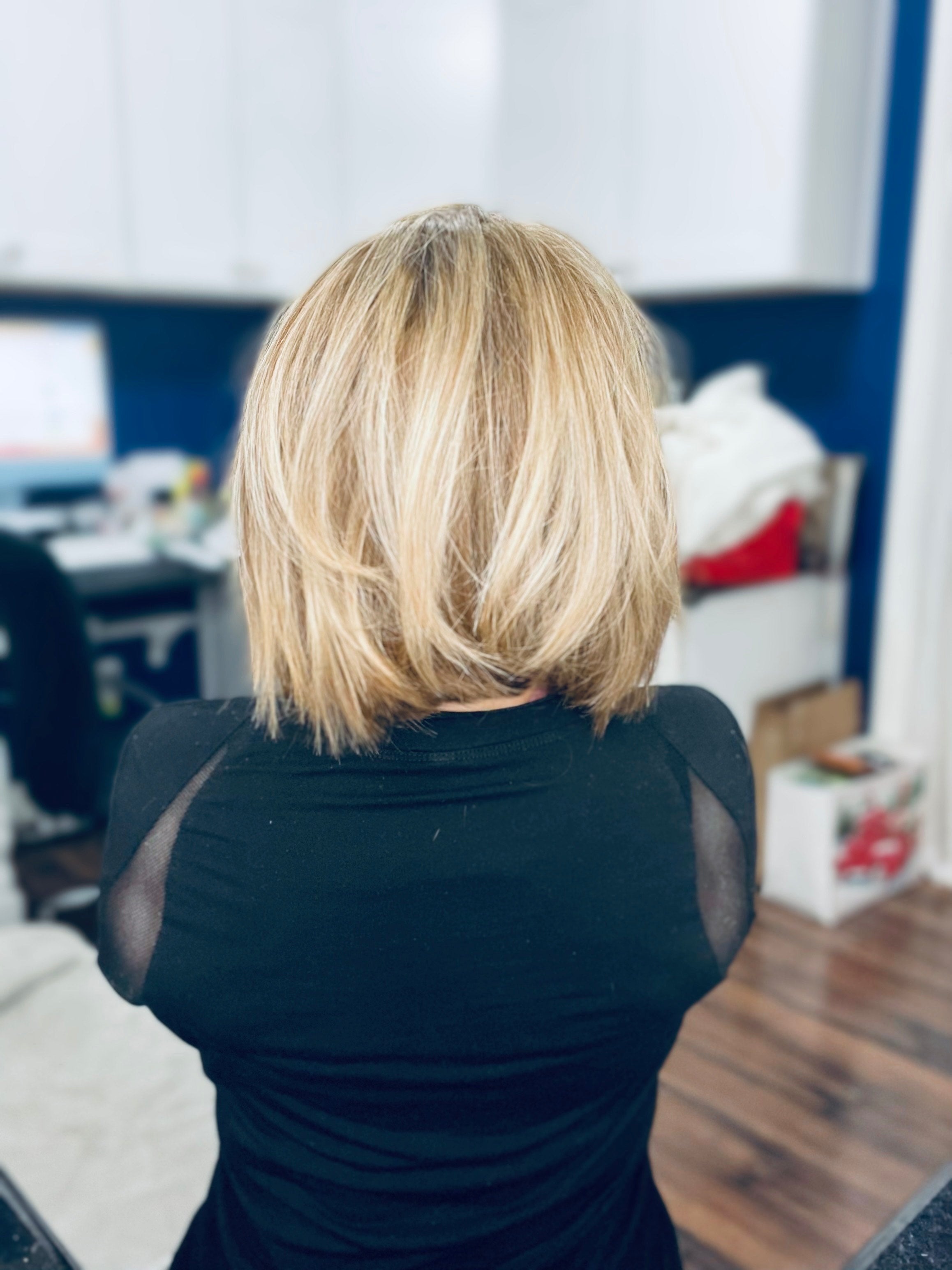 A person with short, layered blonde hair is seen from behind in an office setting, wearing a black shirt.