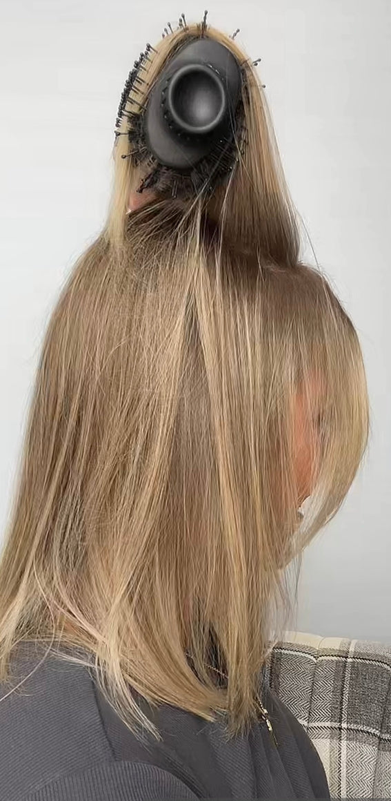 A person is using a round hair dryer with a brush attachment to style their shoulder-length blonde hair.