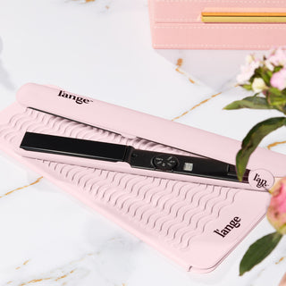 Elegant black hair straightener resting on a textured pink mat and matching box, with floral accents nearby.