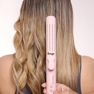 Pink hair styling tool with multiple temperature settings displayed against long, styled hair showing waves and straight sections.