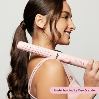 Smiling model with long, wavy ponytail holding a pink Le Duo Grande styling tool.