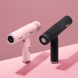 Two L’ange Le Styliste Luxe hair dryers in blush pink and matte black displayed on a pink background. The image highlights both the front nozzle and rear digital display designs.