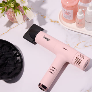 Pink hair dryer with diffuser attachment, grouped alongside various hair care products in sleek bottles, set against a marble surface.