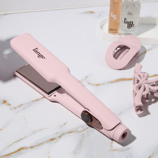 Pink hair straightener set with a modern design, featuring matching accessories and styling products on a marble surface.