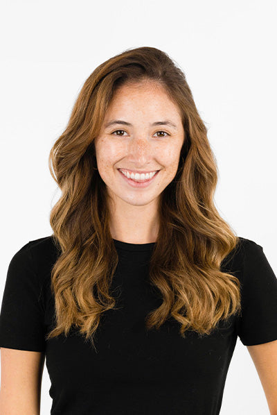 A smiling woman with long, wavy brown hair wearing a black shirt against a plain white background.