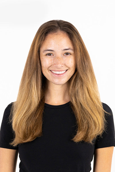 A person with long, light brown hair and freckles, wearing a black shirt, smiles at the camera against a plain white background.