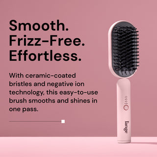 A pink L’ange straightening brush with black ceramic-coated bristles stands upright on a pink background. Text on the left reads: 'Smooth. Frizz-Free. Effortless.' Below, it says: 'With ceramic-coated bristles and negative ion technology, this easy-to-use brush smooths and shines in one pass.