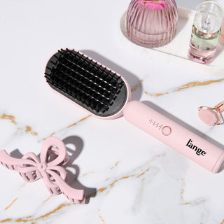Blush L’ange heated brush displayed on a marble surface with hair clip and beauty accessories.