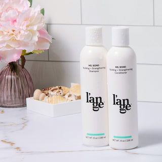 Ms. Bond bundle on a a vanity table. Bundle shows one bottle of Ms. Bond Building + Strengthening Shampoo and one bottle of Ms. Bond Building + Strengthening Conditioner