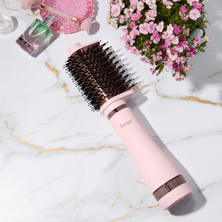 Blush and rose gold L’ange round brush styling tool on a marble surface with flowers and beauty items. 65MM