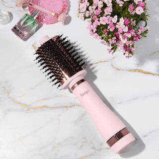 Blush and rose gold L’ange round brush styling tool on a marble surface with flowers and beauty items. 75MM