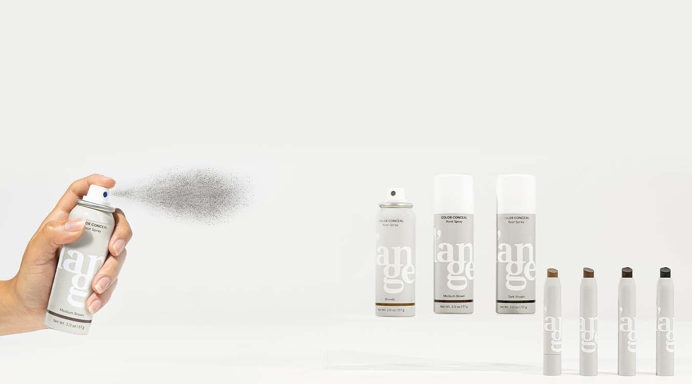 A hand spraying a can of root concealer with other cans and applicators lined up beside it, displaying a range of hair touch-up products.